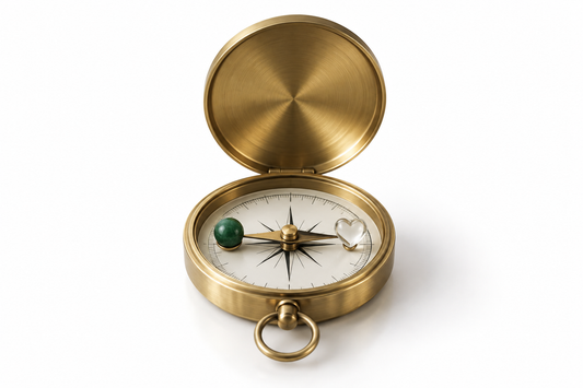 Brass compass balanced between a green stone and clear glass heart on a white background, symbolizing responsible freedom