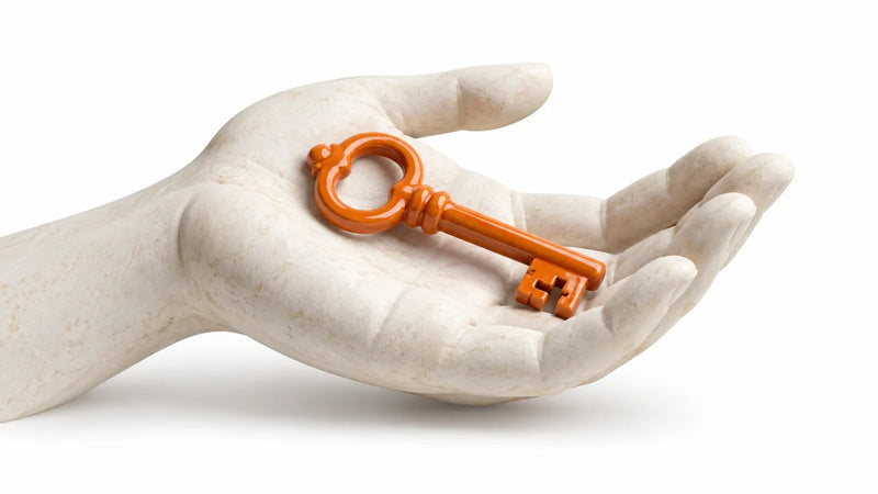 An orange ceramic key resting in an open ivory hand sculpture